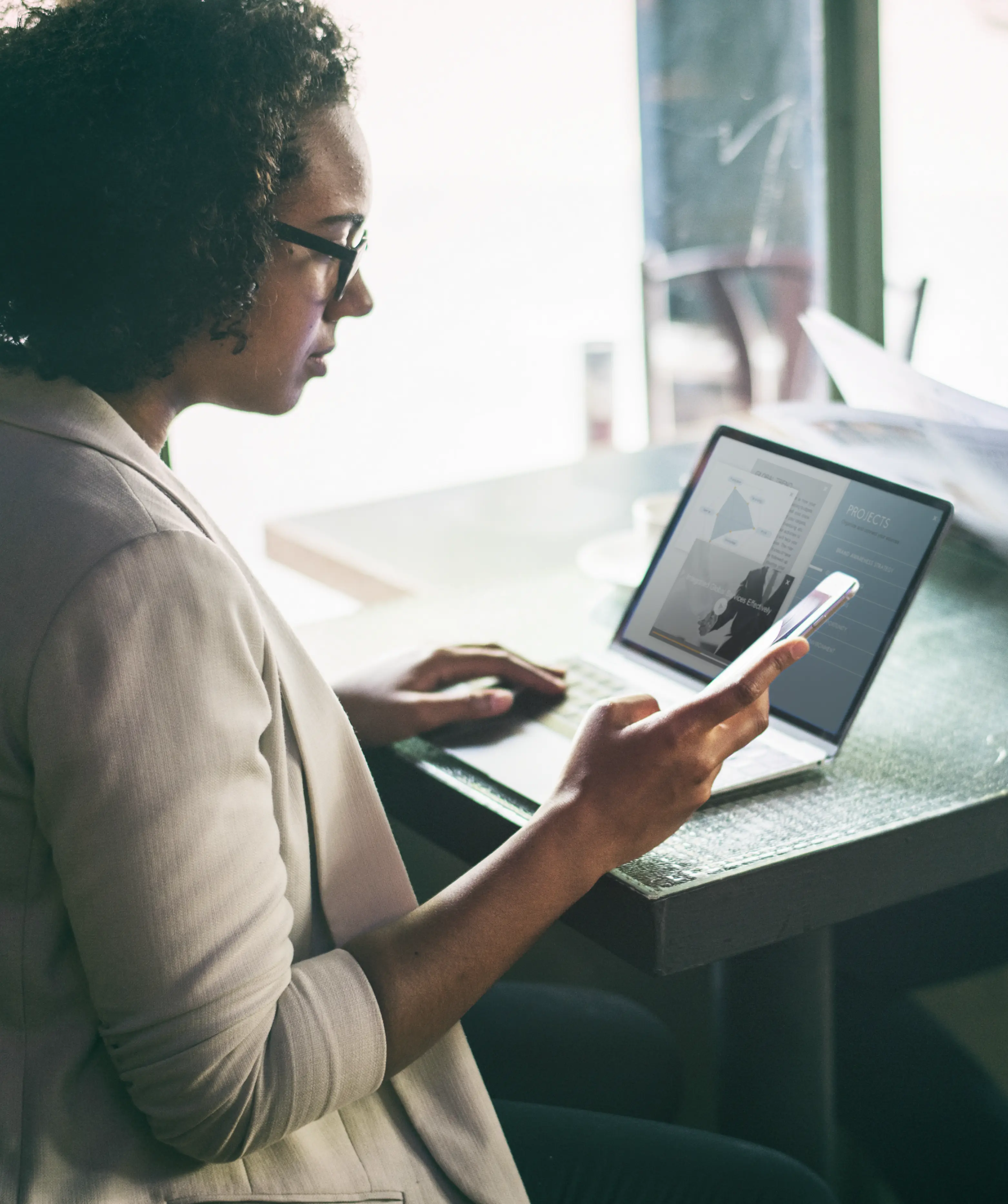 Une femme qui regarde son smartphone en travaillant sur son ordinateur portable